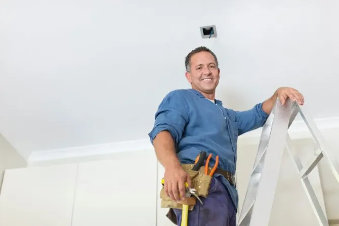 Electrician on ladder fixing ceiling light.