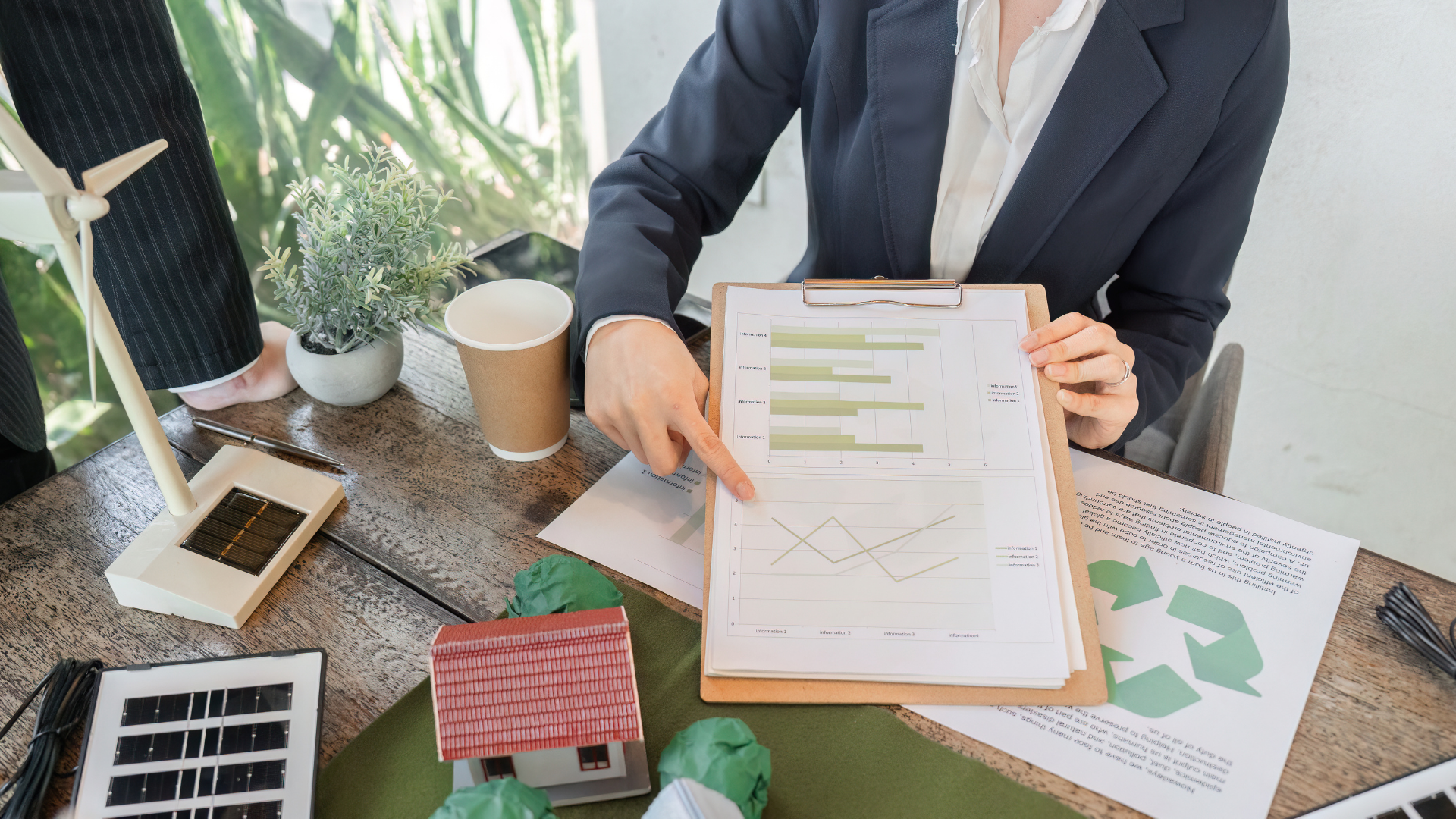 A woman is sitting at a desk holding a clipboard and pointing at a graph.