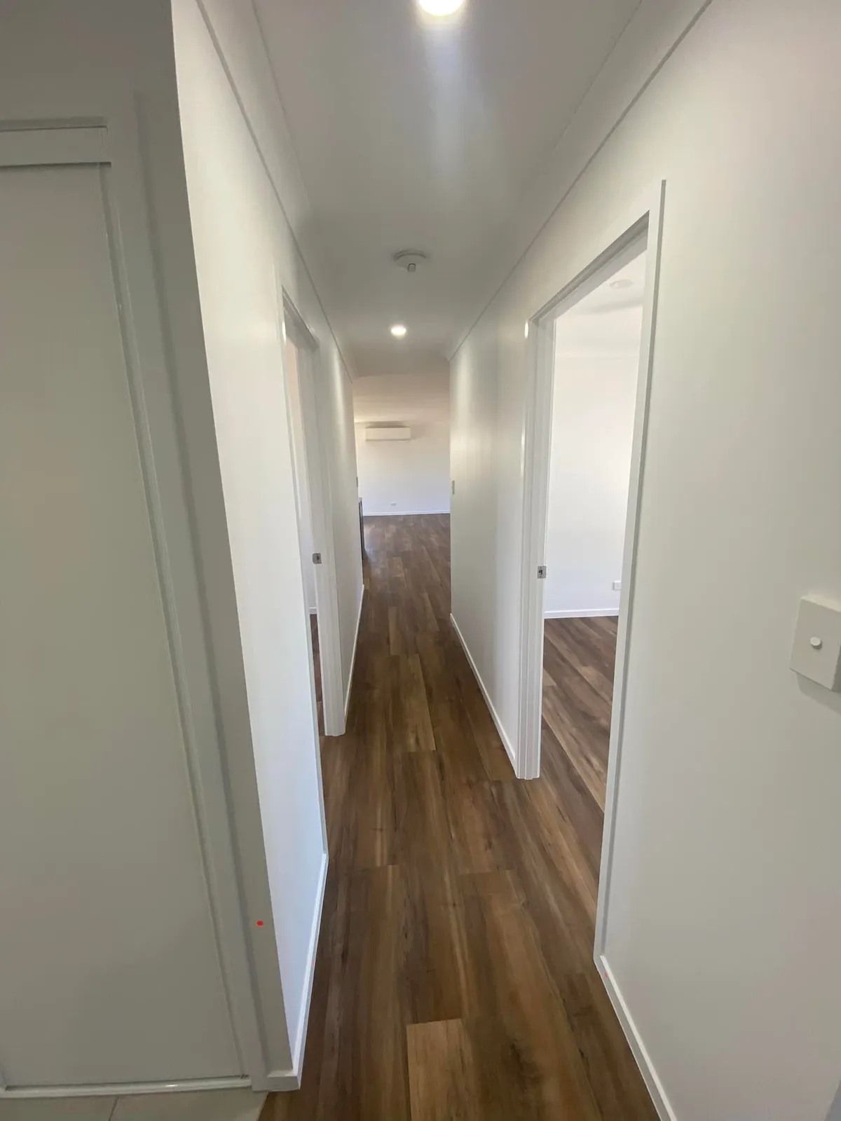 A Hallway with White Walls, Dark Wood-Look Flooring — Country to Coast Homes In Gregory River, QLD