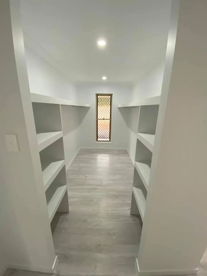 A Pantry with Light-Colored Shelves Lining Both Walls, a Wood-Framed Window at The End — Country to Coast Homes In Gregory River, QLD