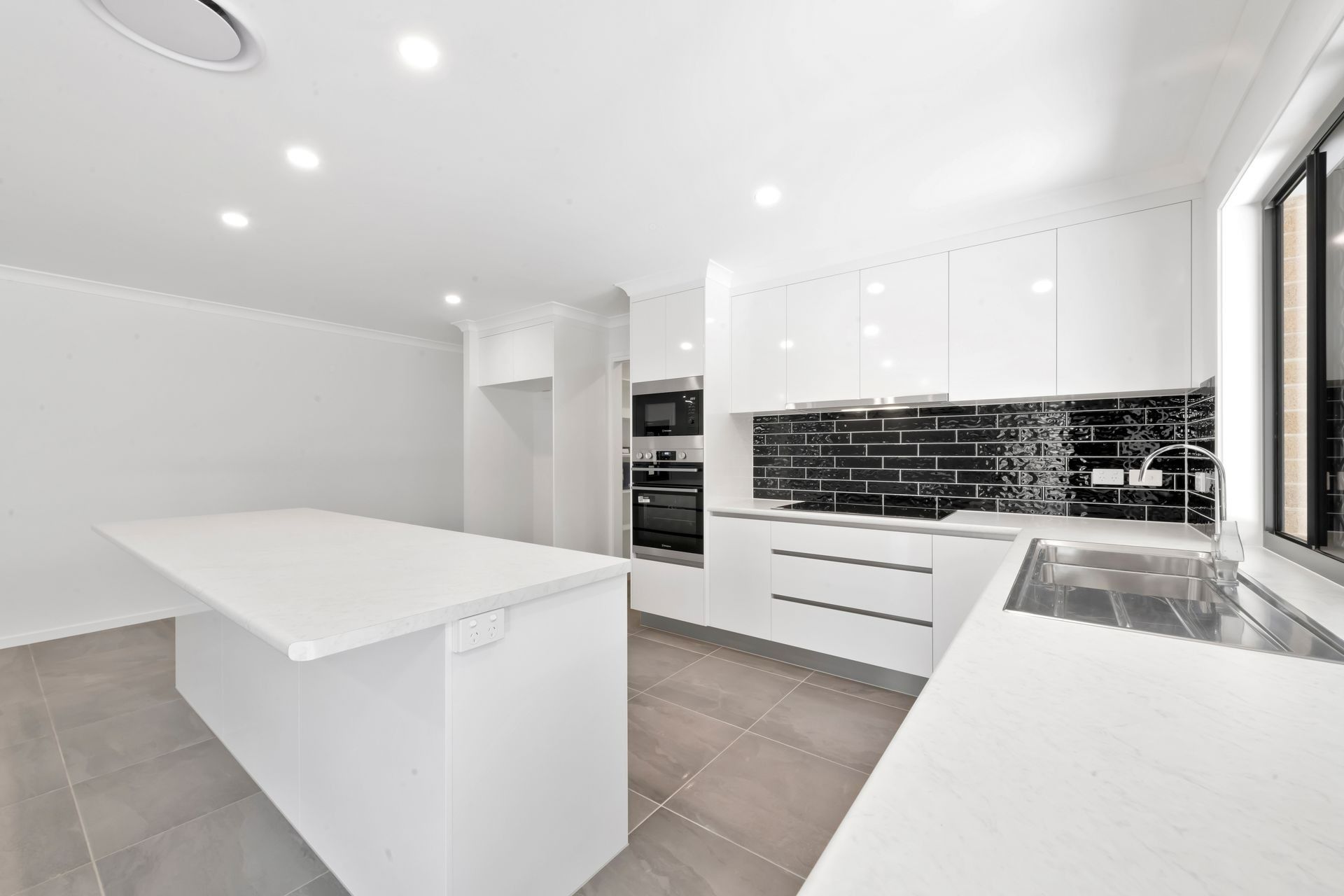 Modern White Kitchen with An Island and Black Backsplash — Country to Coast Homes In Gregory River, QLD
