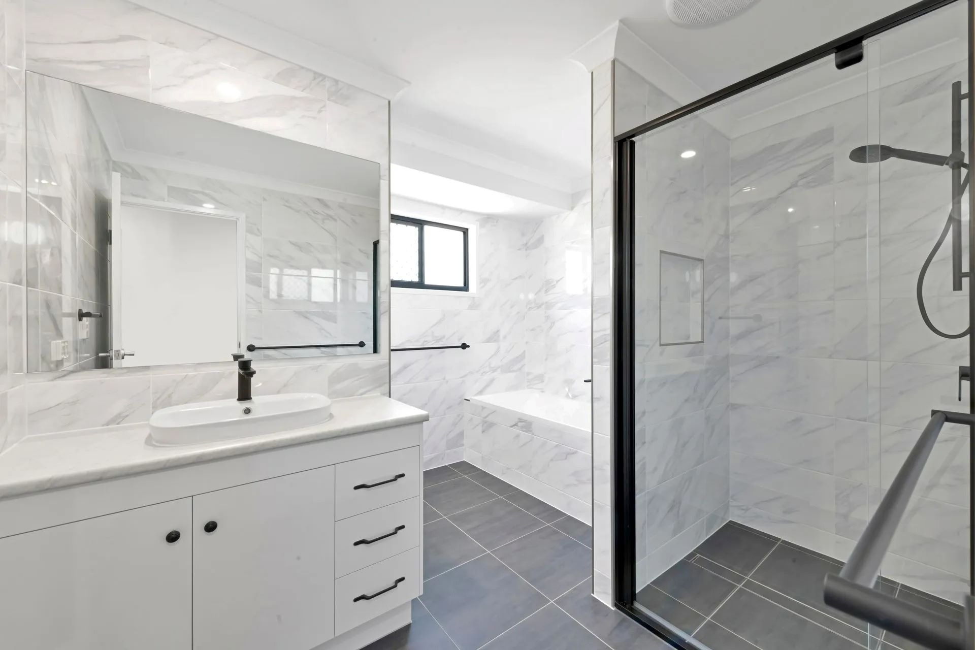 Modern Accessible Bathroom with White Marble-Look Tiles, a Glass Shower Enclosure — Country to Coast Homes In Gregory River, QLD