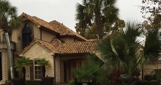 Worker kneeling on a red tile roof, repairing shingles under a blue sky