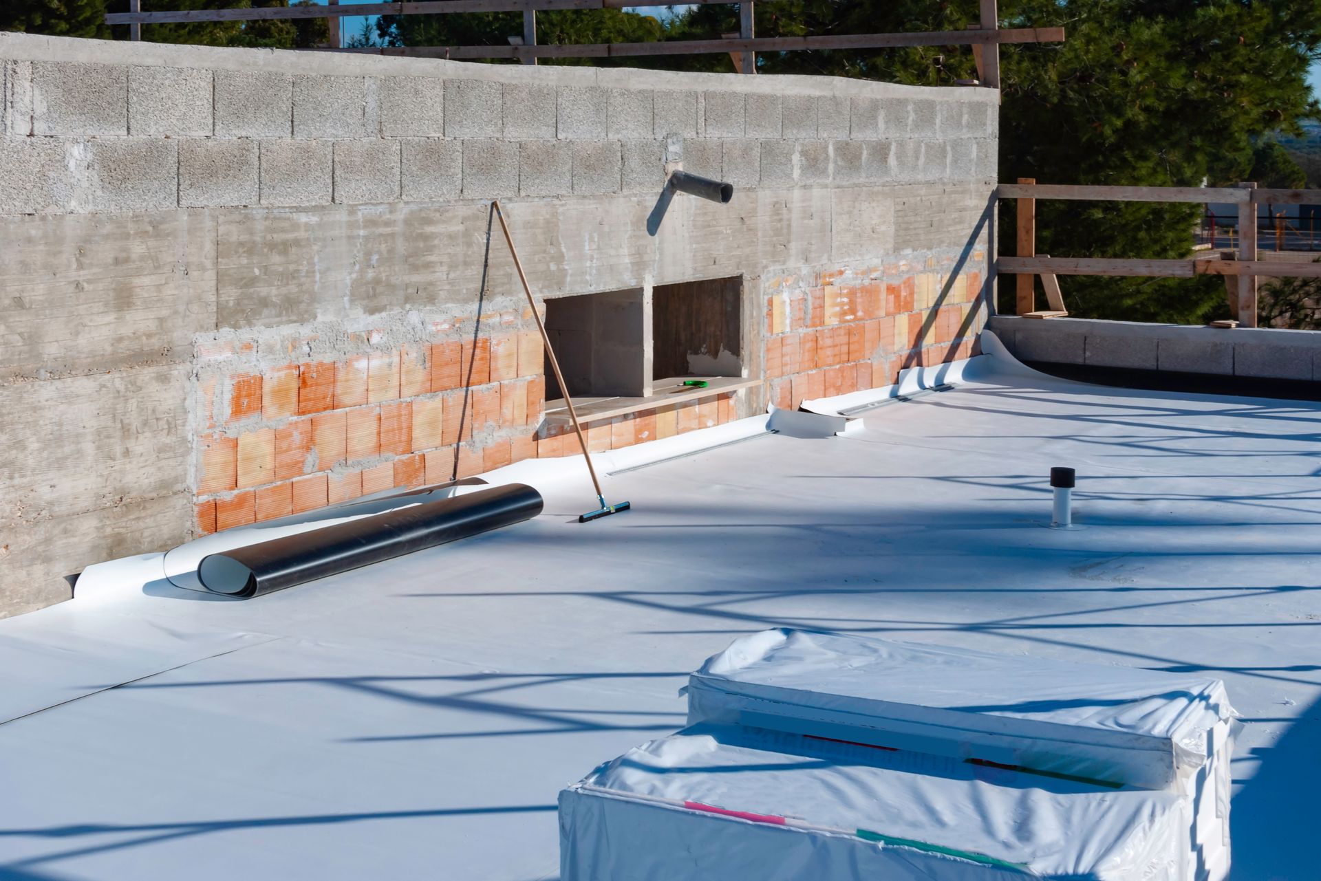 Rooftop with a concrete wall, exposed brick patch, and blue waterproofing membrane under construction