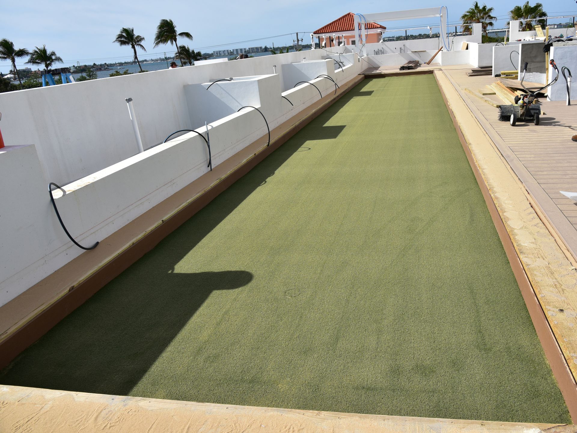 Narrow green turf walkway on a rooftop beside white walls and ocean views
