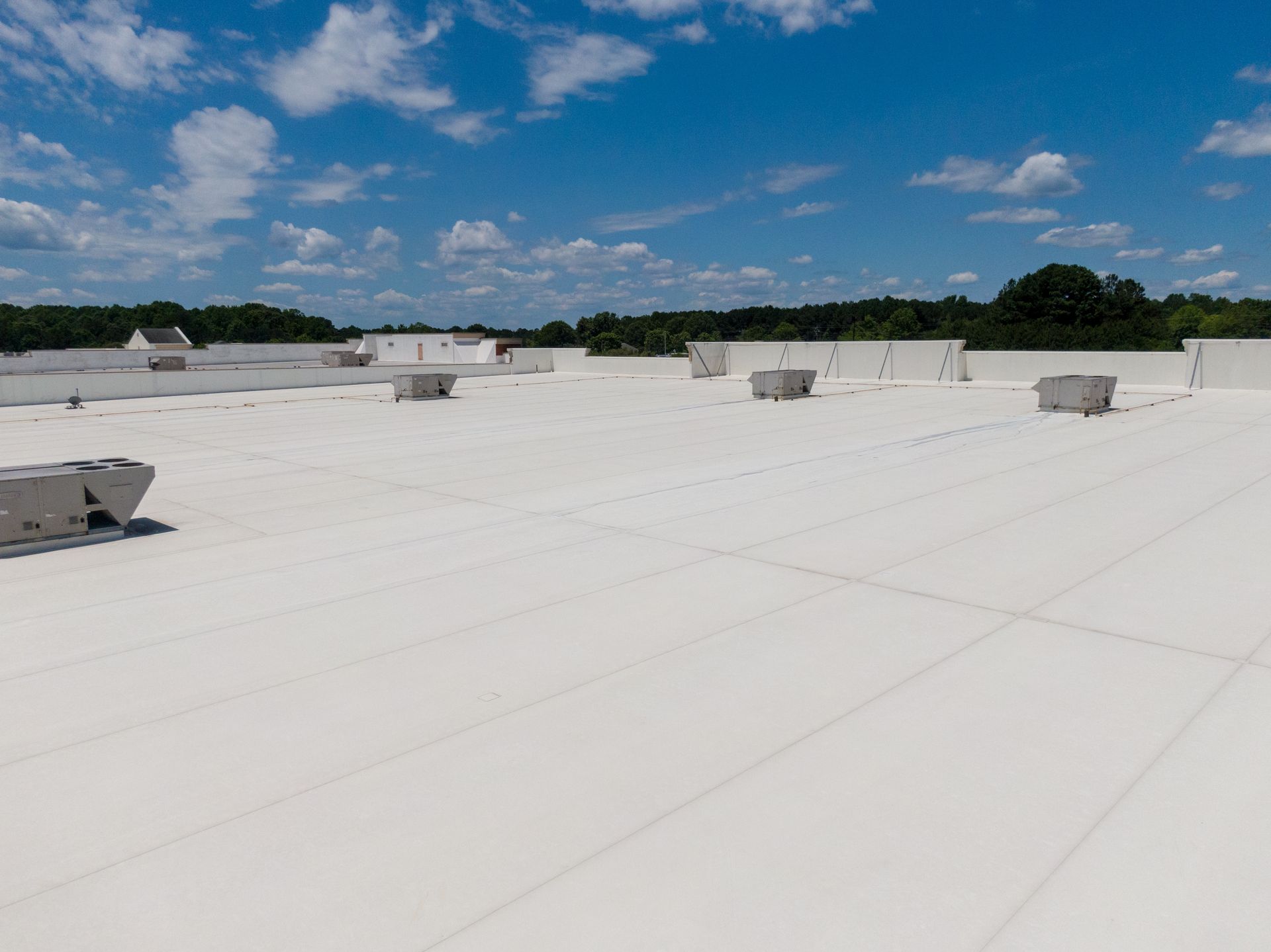 White flat rooftop with vents under a blue sky with scattered clouds