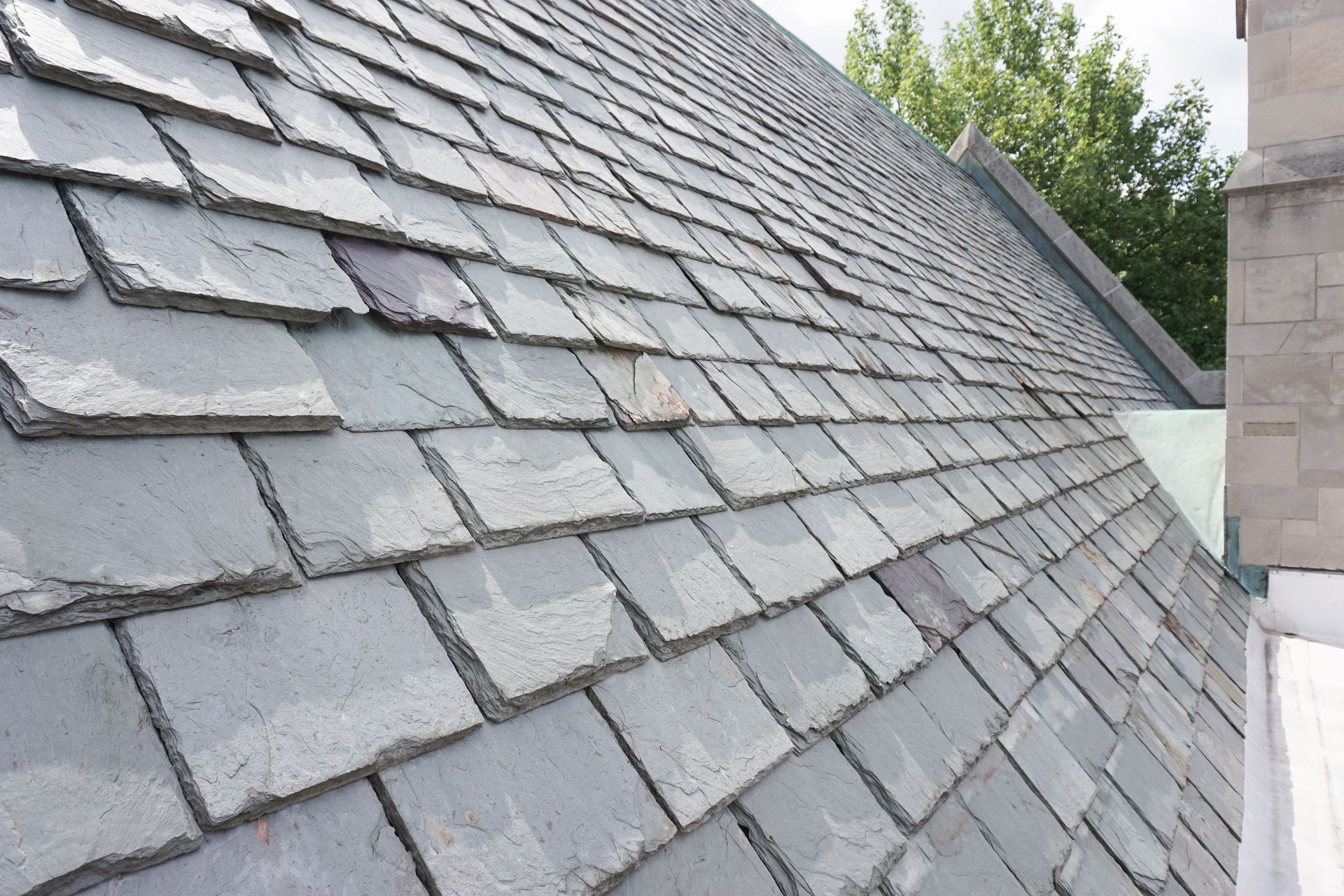 Gray slate roof with overlapping shingles and a small stone chimney on the right