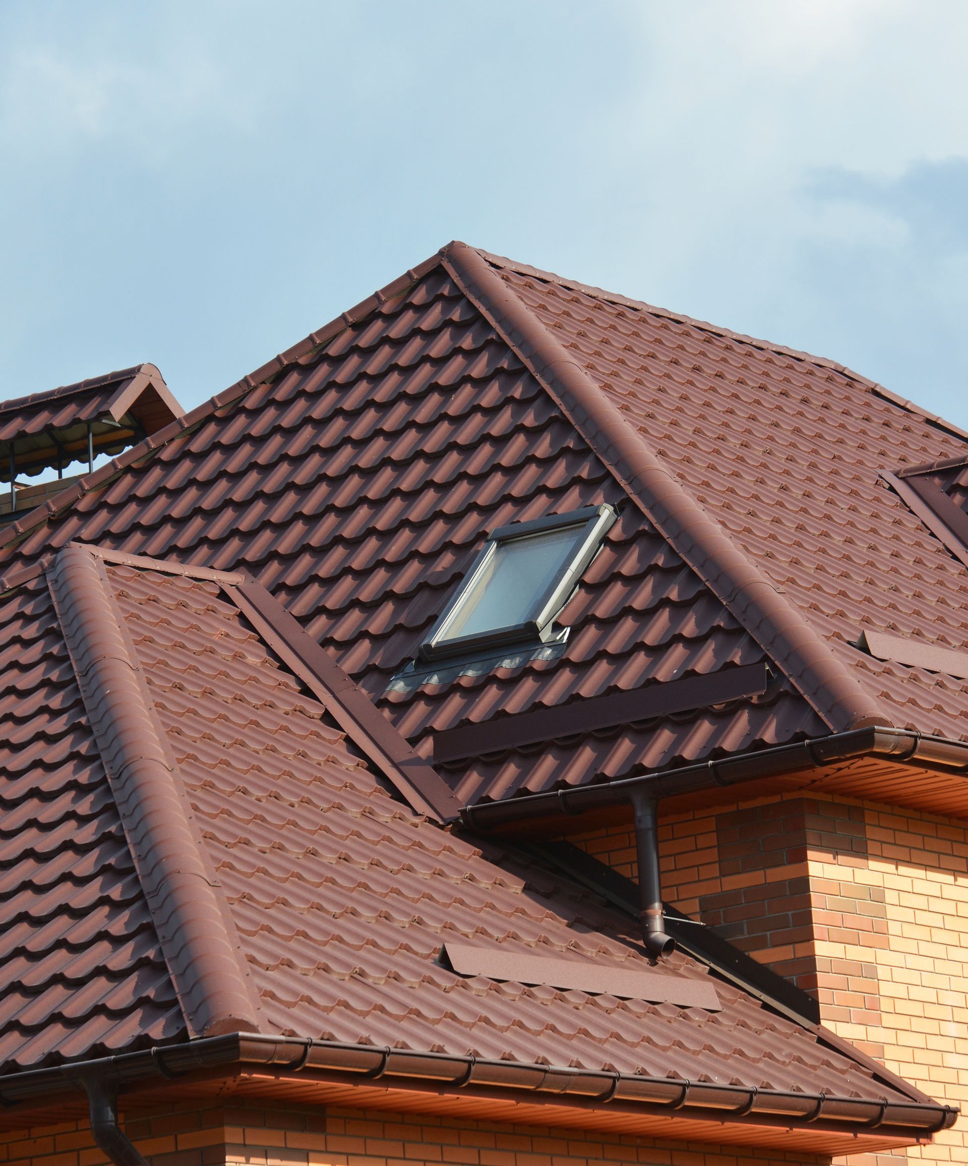 Brown tiled house roof with a skylight against a blue sky
