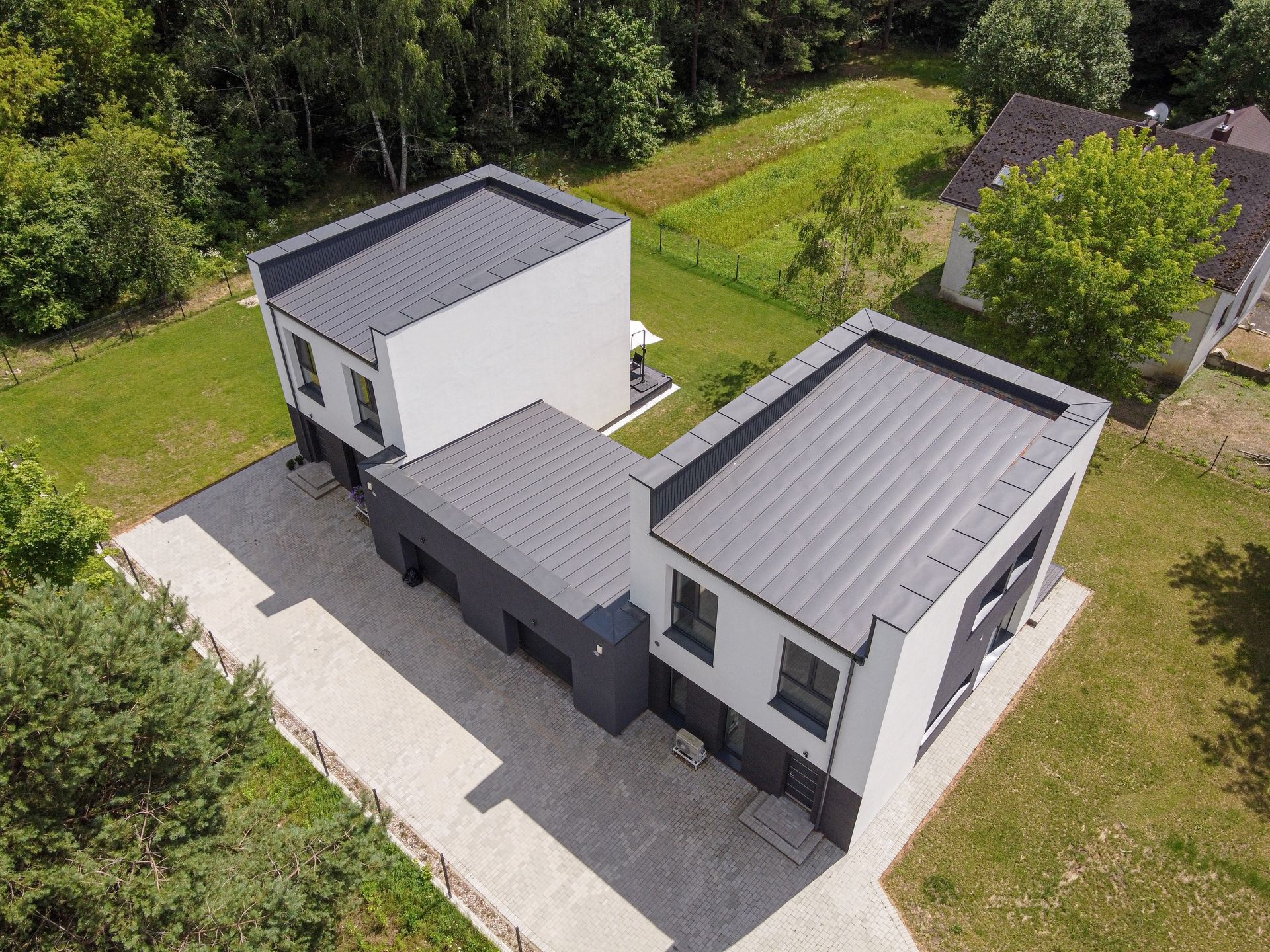 Aerial view of a modern white-and-gray house with a flat roof, surrounded by grass and trees.
