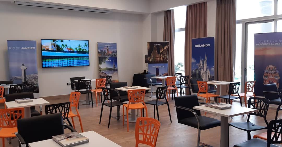 A room with tables and chairs and a flat screen tv on the wall.