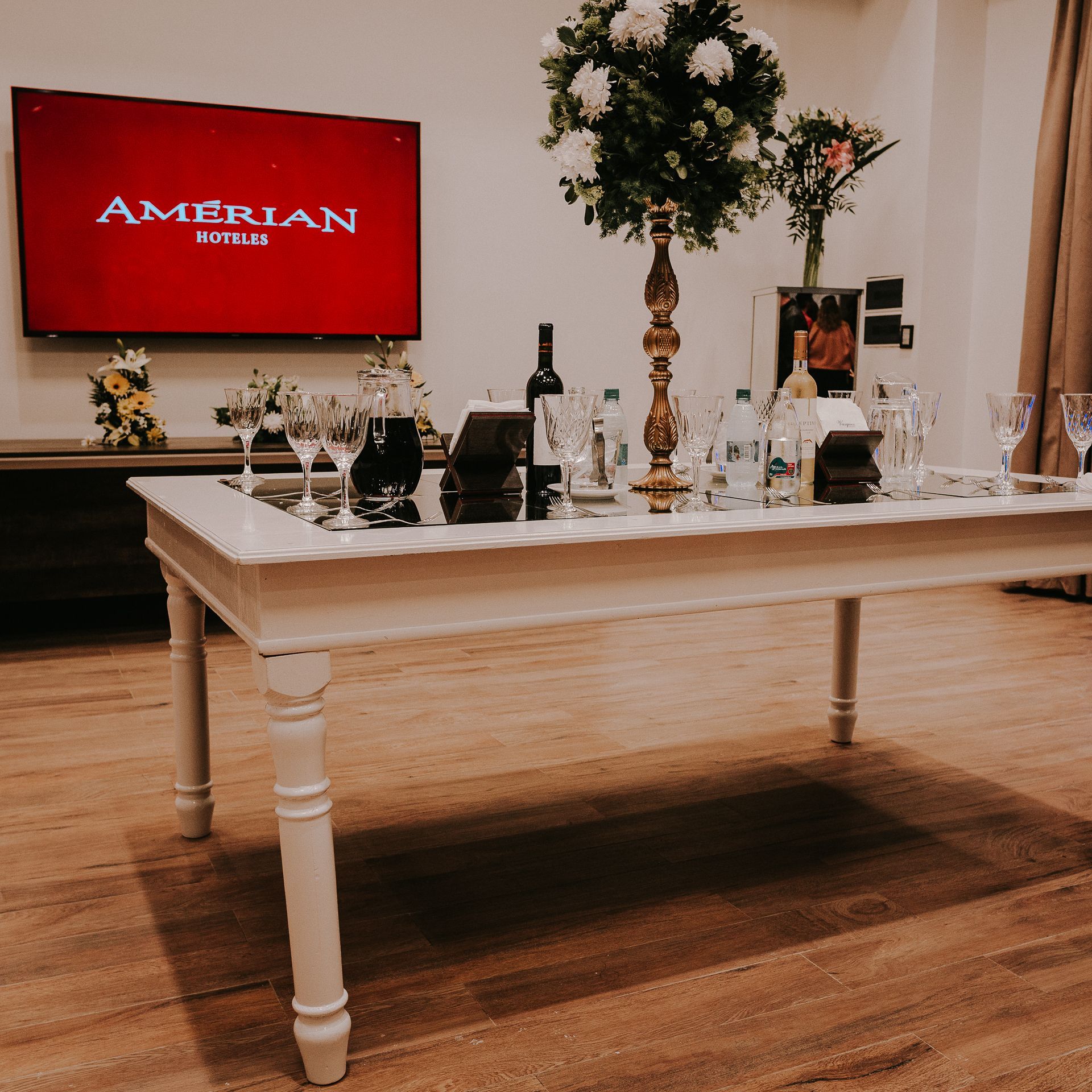 A table with a vase of flowers in front of a television that says amerian