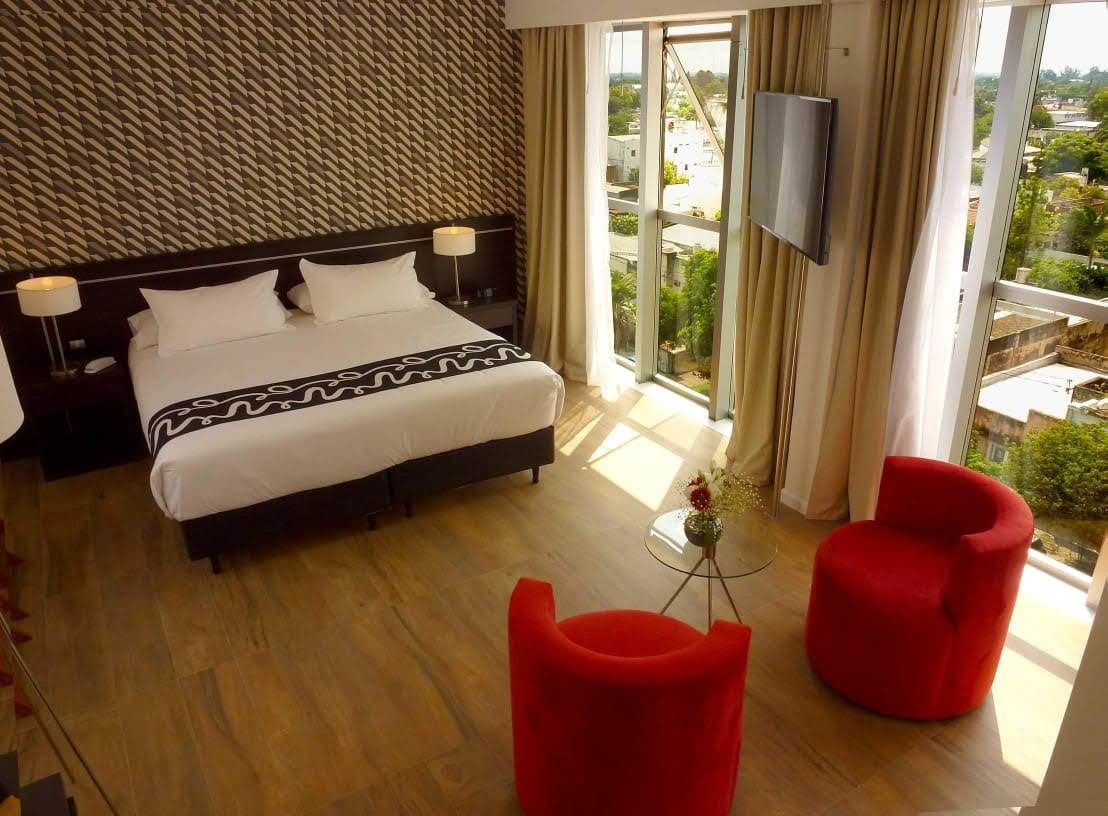 A hotel room with a king size bed and two red chairs