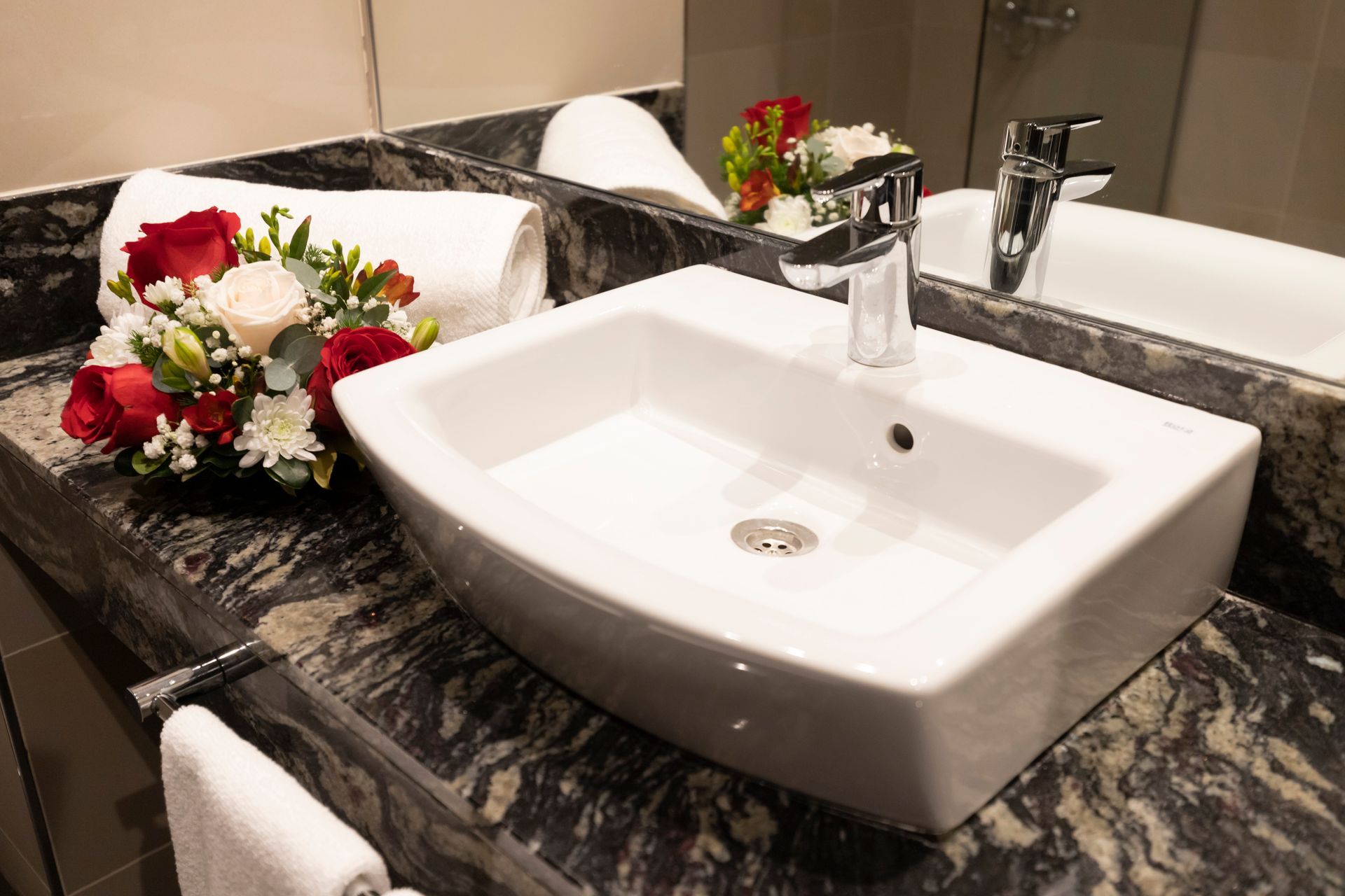 A bathroom sink with a mirror and flowers on the counter.
