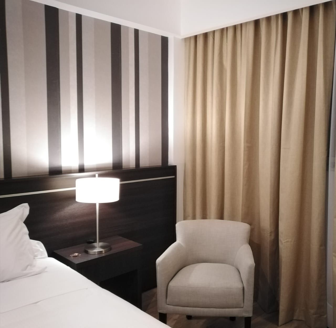 A hotel room with a bed a chair and a lamp