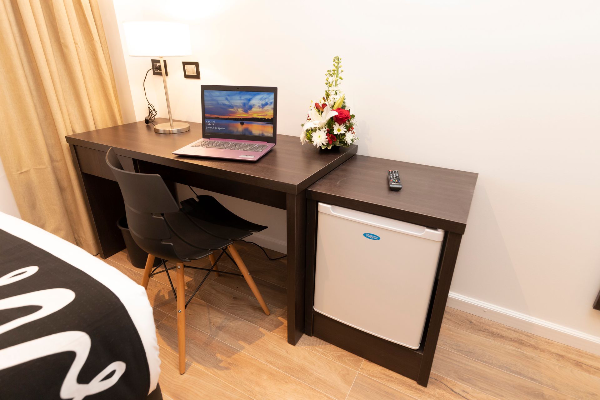 A hotel room with a desk , chair , laptop and refrigerator.