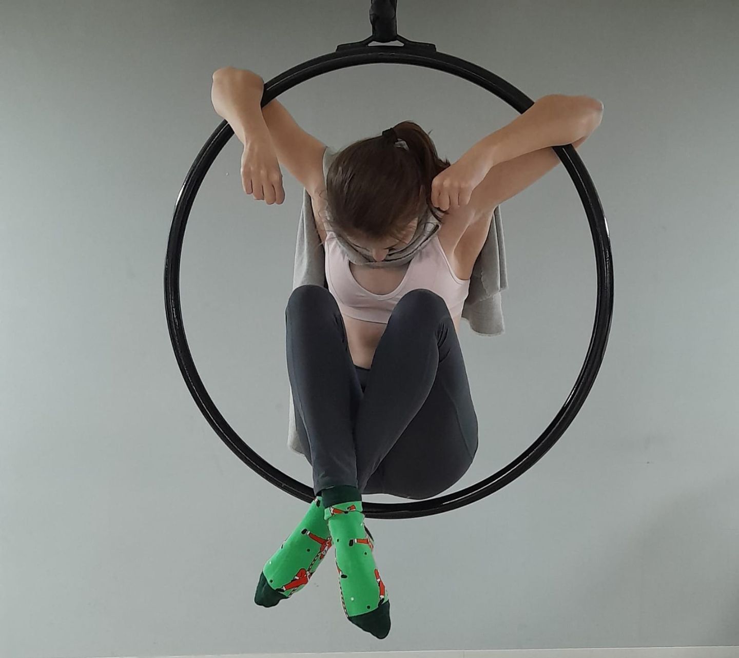 An individual seated in a hoop, captured from the front, demonstrating a balance pose with legs crossed and feet flexed.