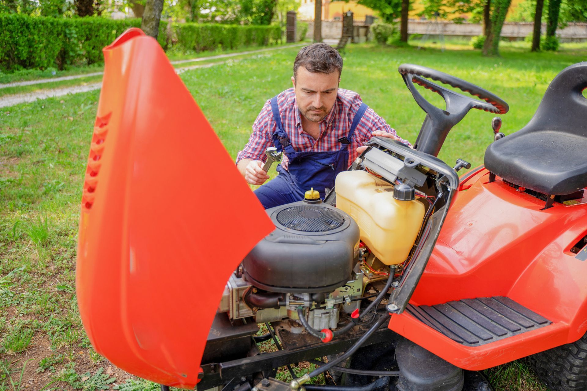 A man is working on a lawn mower with its hood open.