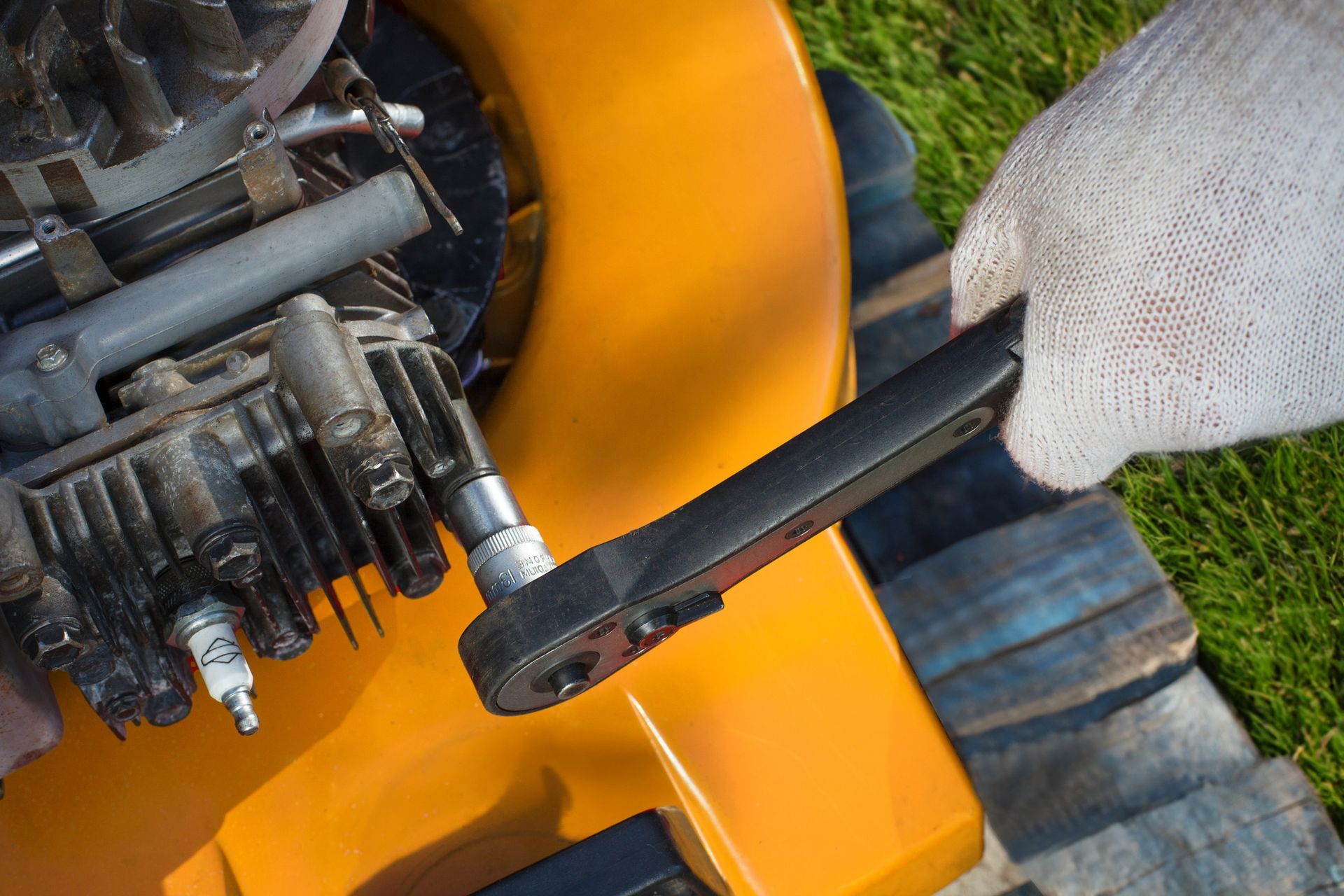 A person is fixing a lawn mower with a wrench.