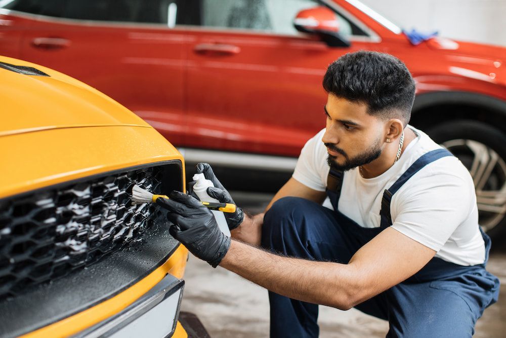 A Man Is Cleaning the Grille of A Yellow Car in A Garage — Wyong Radiator Repairs in Tuggerah, NSW