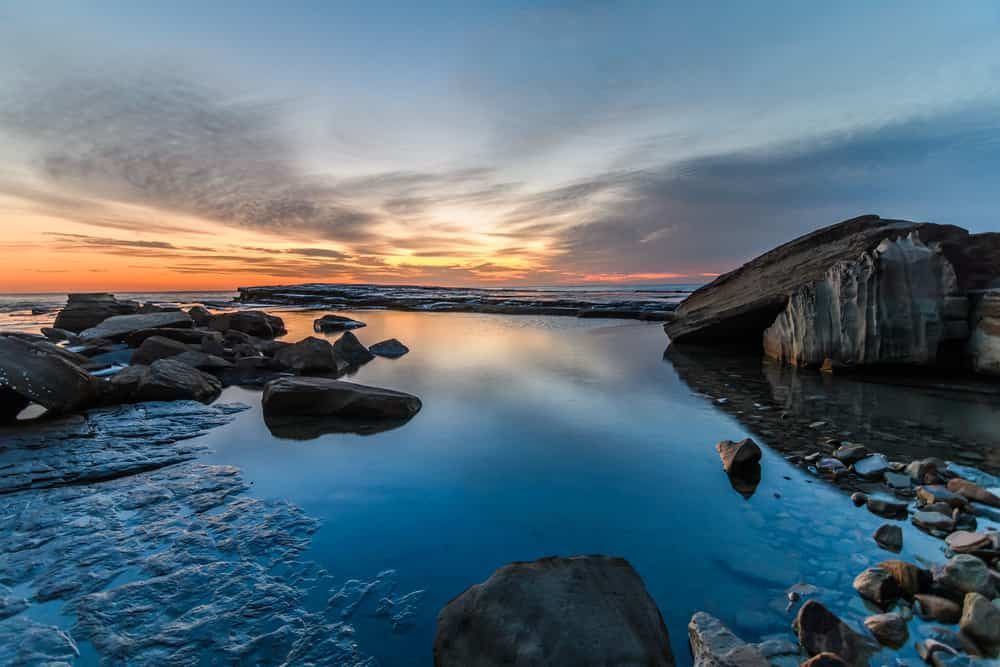 A Sunset Over a Body of Water With Rocks in the Foreground — Wyong Radiator Repairs In Terrigal, NSW