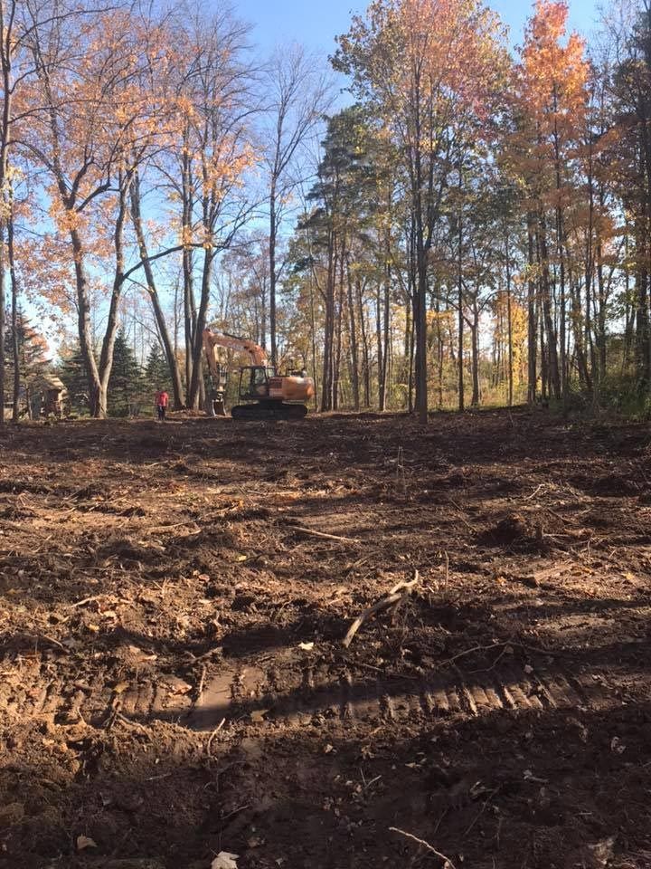 A bulldozer is moving dirt in a field with trees in the background.