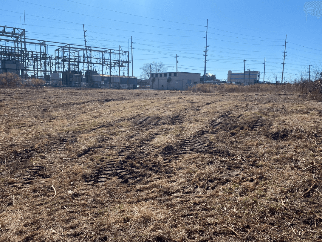 A field of dry grass with a power station in the background.