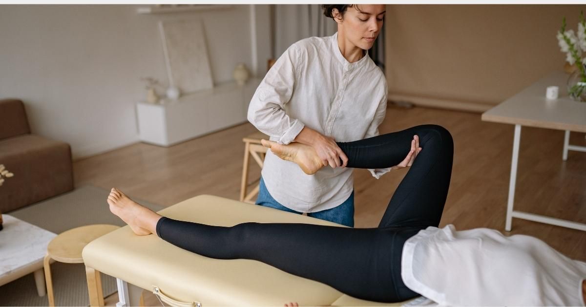 Therapist stretching a person's leg on a massage table indoors.