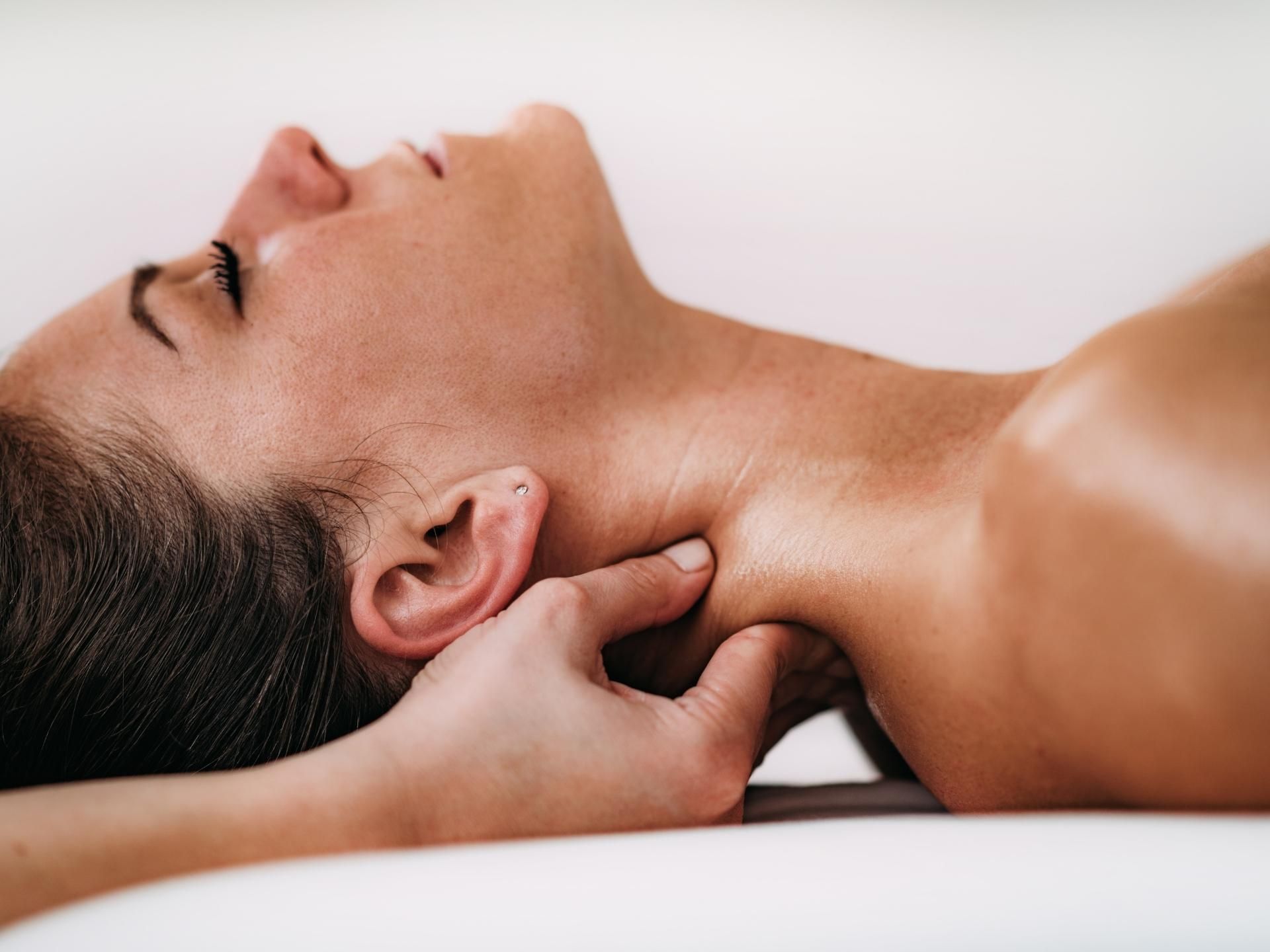 Hands gently massage the neck of a reclining person on a white surface.