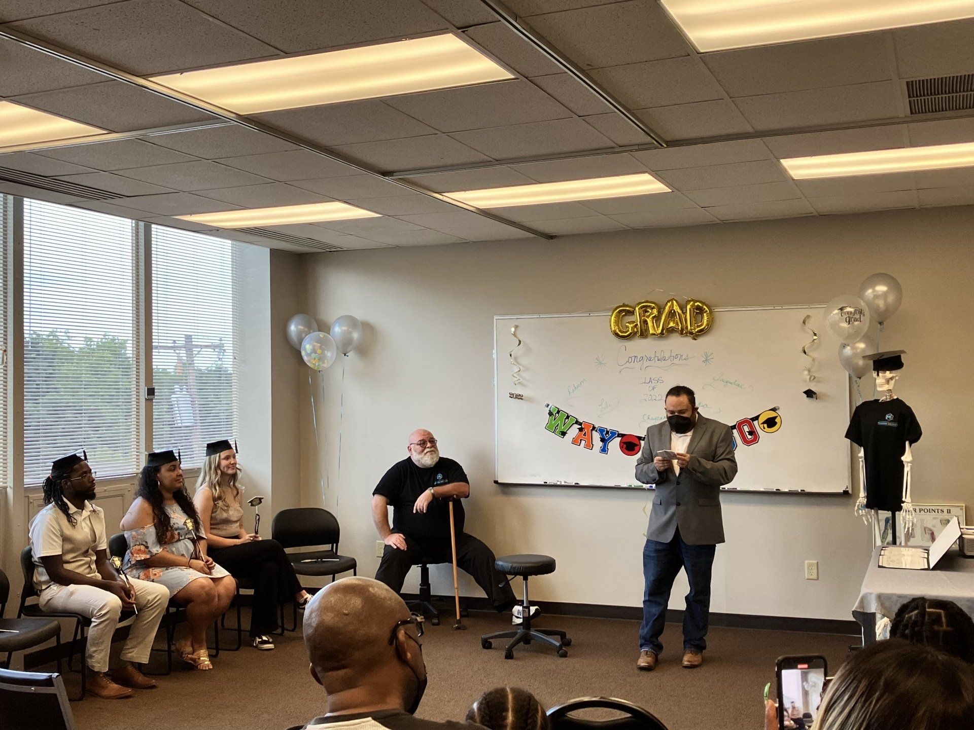 A man is standing in front of a group of massage institute graduates.