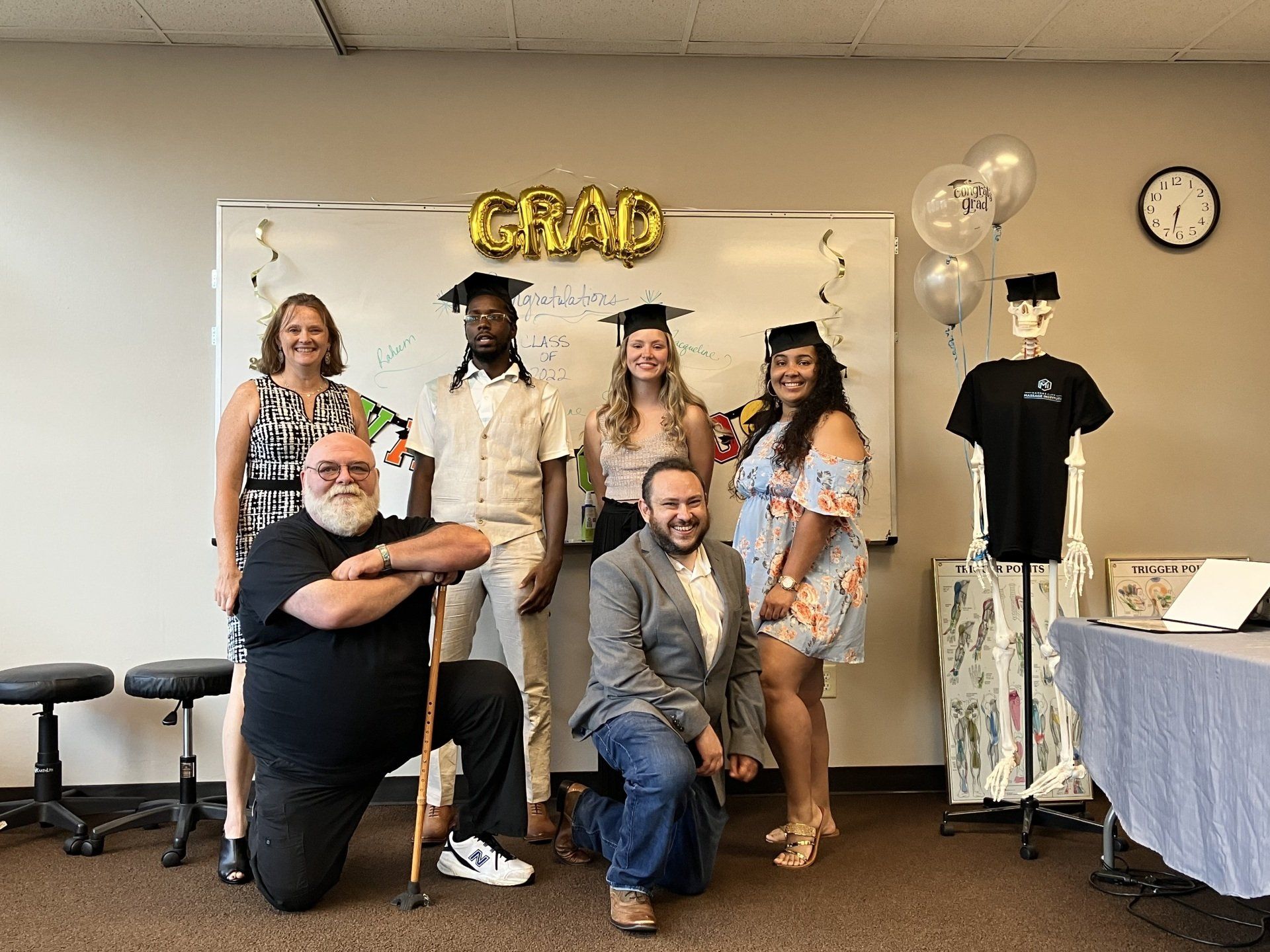 A group of massage therapy graduates are posing for a picture in front of a white board.