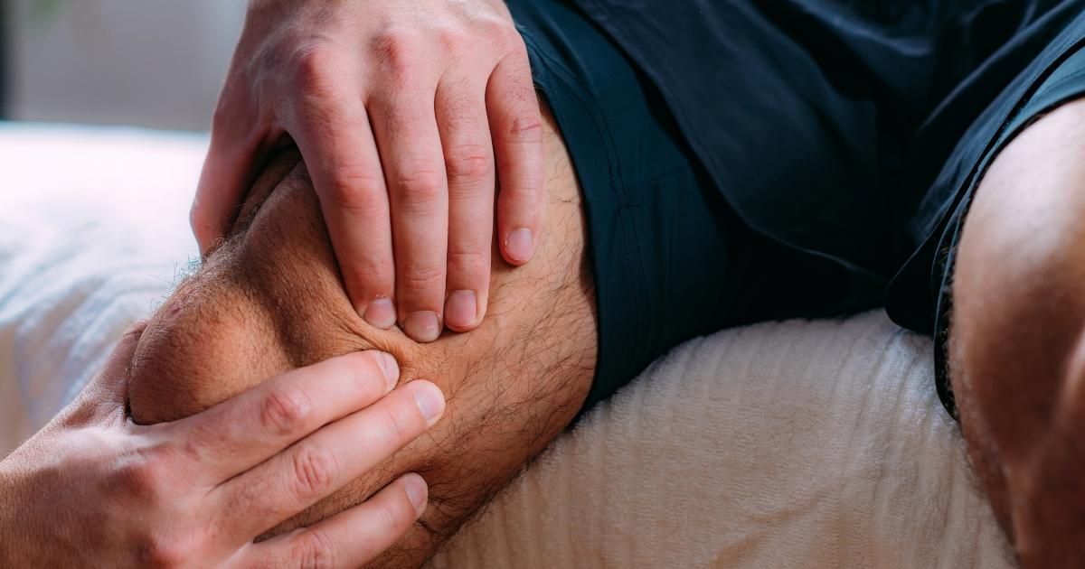 Person holding their knee, possibly in pain, while sitting on a bed.