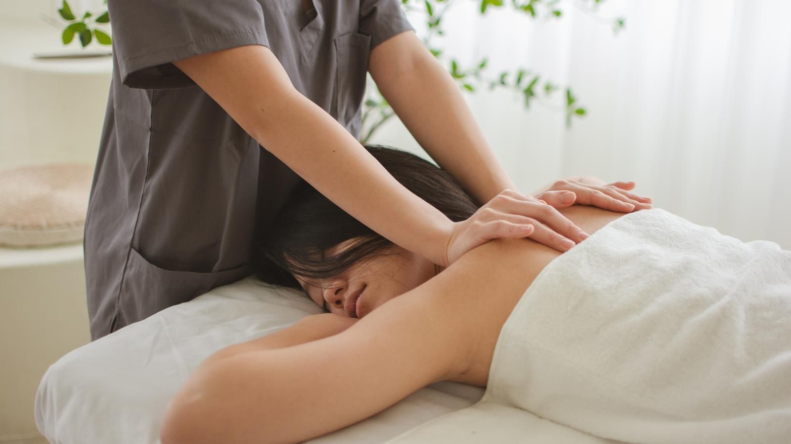 A massage student is standing next to a massage table in a spa.