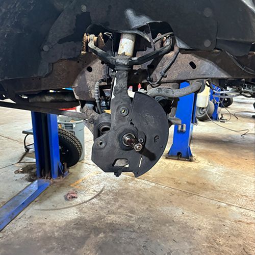 Front suspension of a vehicle on a lift, showing the hub, brake rotor, and control arms | S&C Automotive Inc