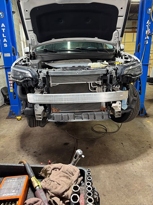 White car on a lift in a garage with the front bumper removed, revealing the engine components  | S&C Automotive Inc