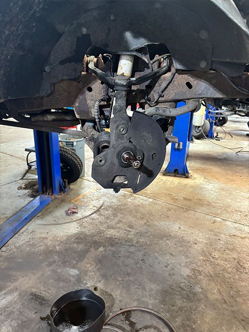 Front suspension and wheel components of a vehicle being worked on in a garage, lifted on a blue hydraulic lift  | S&C Automotive Inc