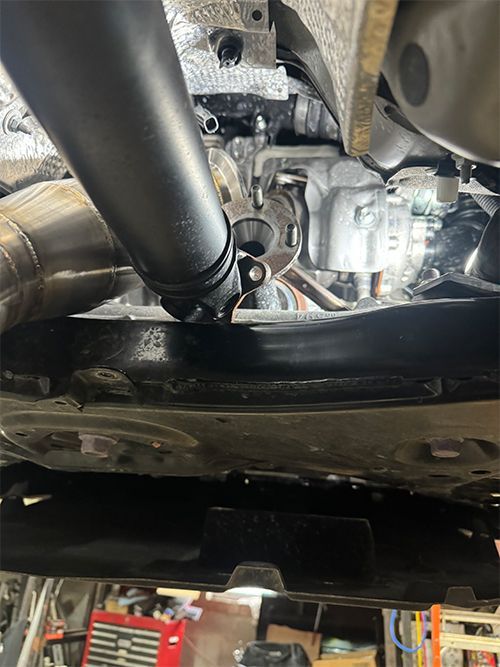 Undercarriage view with a black exhaust pipe and engine components; a car repair setting  | S&C Automotive Inc