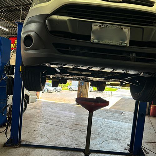 Van on a lift in a garage, with an oil drain pan underneath | S&C Automotive Inc