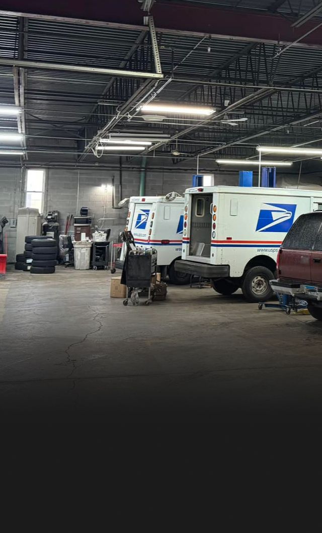 Inside a vehicle repair shop, postal service trucks are parked, worker  | S&C Automotive Inc