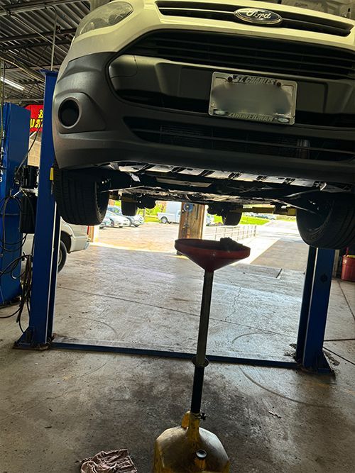 Ford van on a lift undergoing an oil change in an auto repair shop. Oil drain pan is beneath  | S&C Automotive Inc
