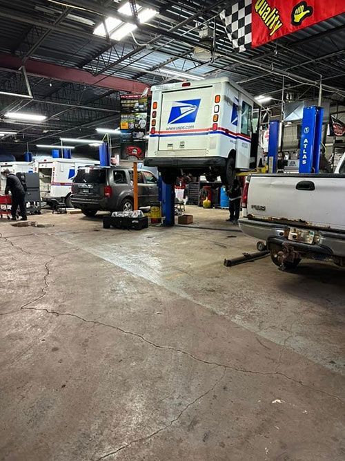 A United States Postal Service vehicle raised on a lift inside a mechanic shop  | S&C Automotive Inc