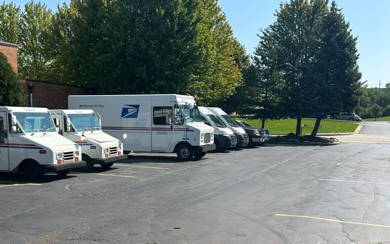 US Postal Service vehicles parked outside, sunny day, surrounded by trees | S&C Automotive Inc