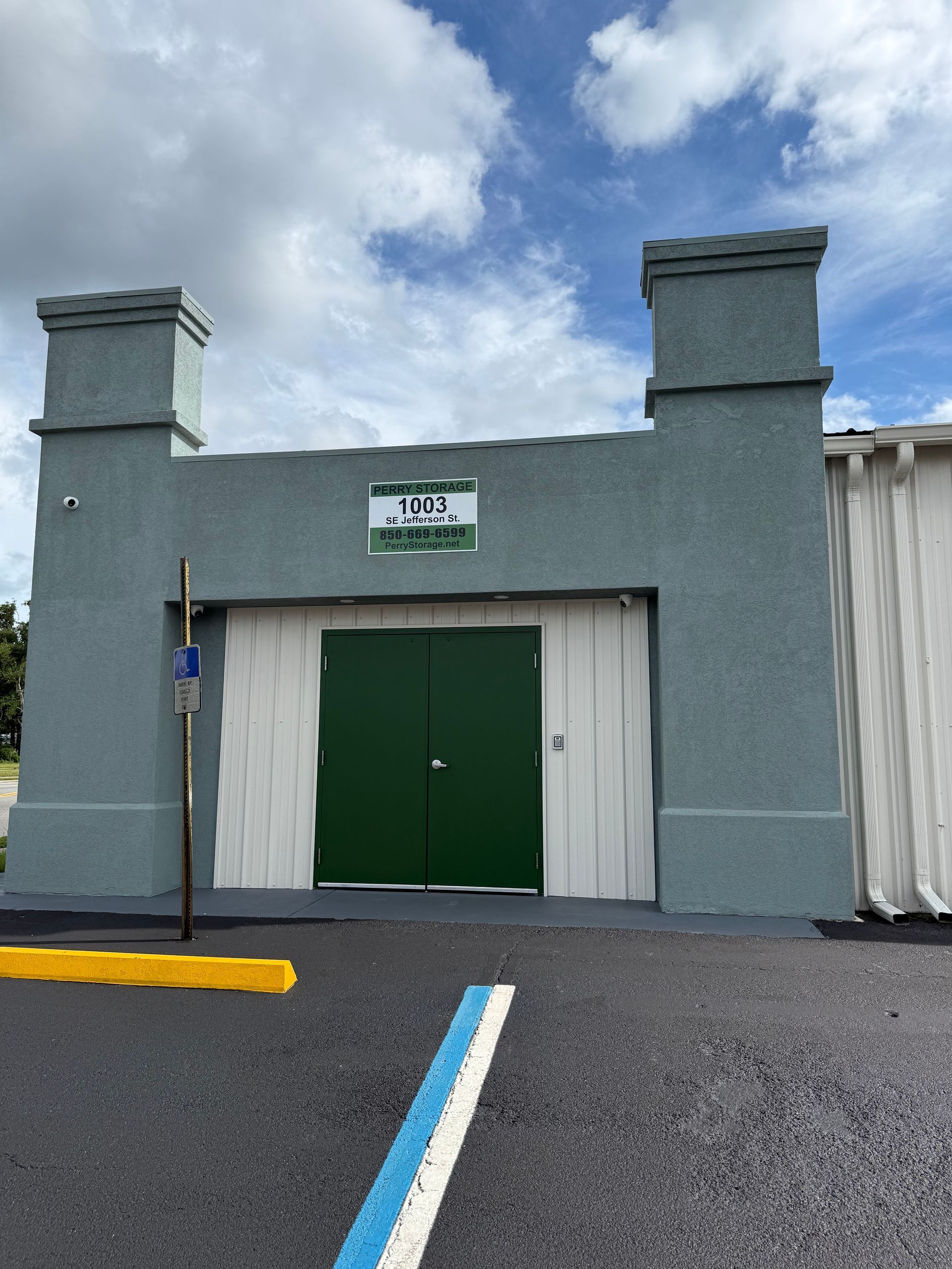 Exterior of a green and white building with a double door entrance and two decorative pillars. Parking lot in front.