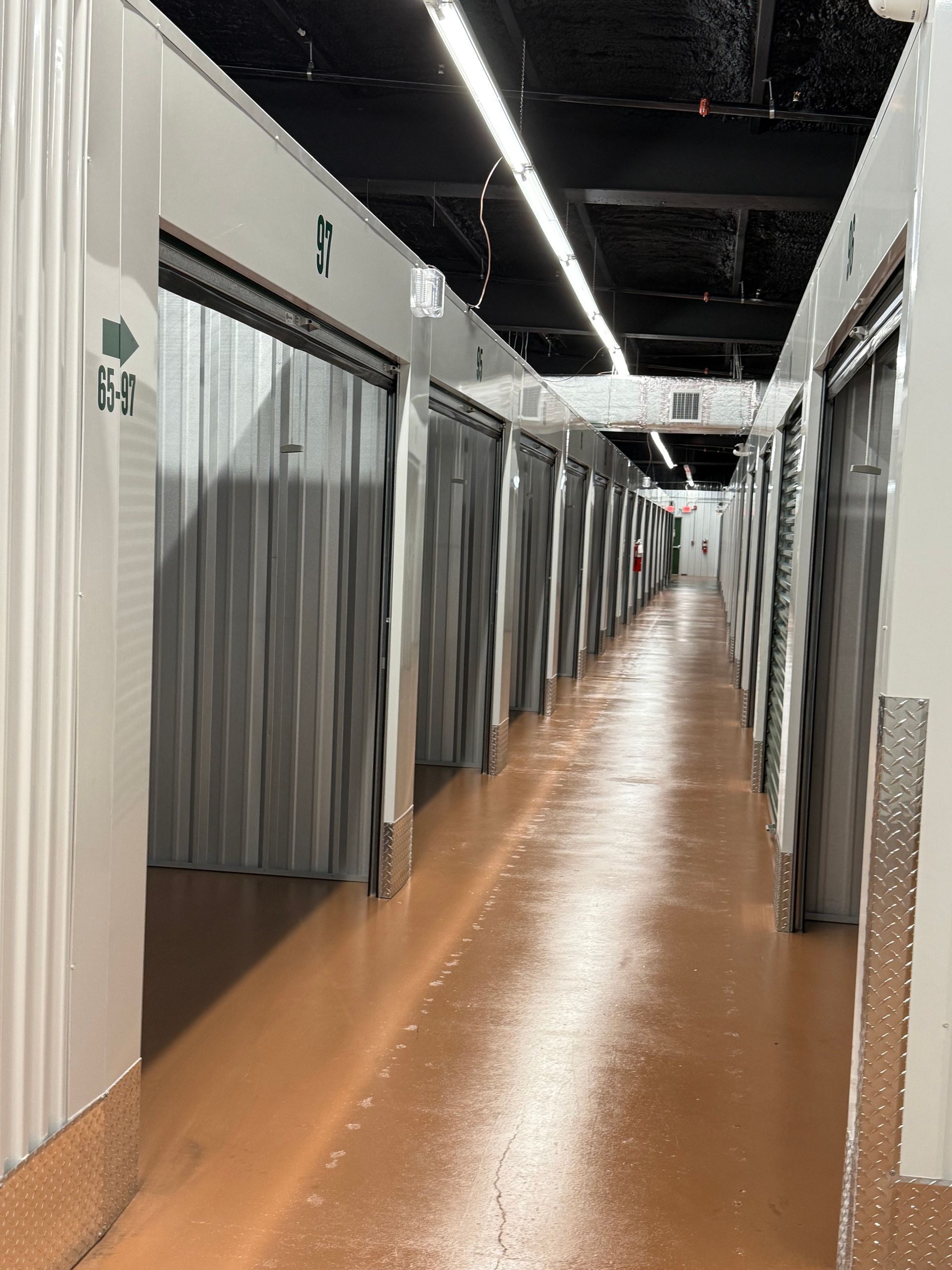 Interior view of a storage facility hallway with many metal unit doors and orange flooring.