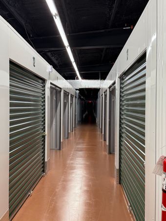Hallway of storage units with green doors, white frames, and red flooring.