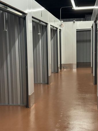 A storage facility hallway with units covered by gray, corrugated curtains. Brown floor, white walls.