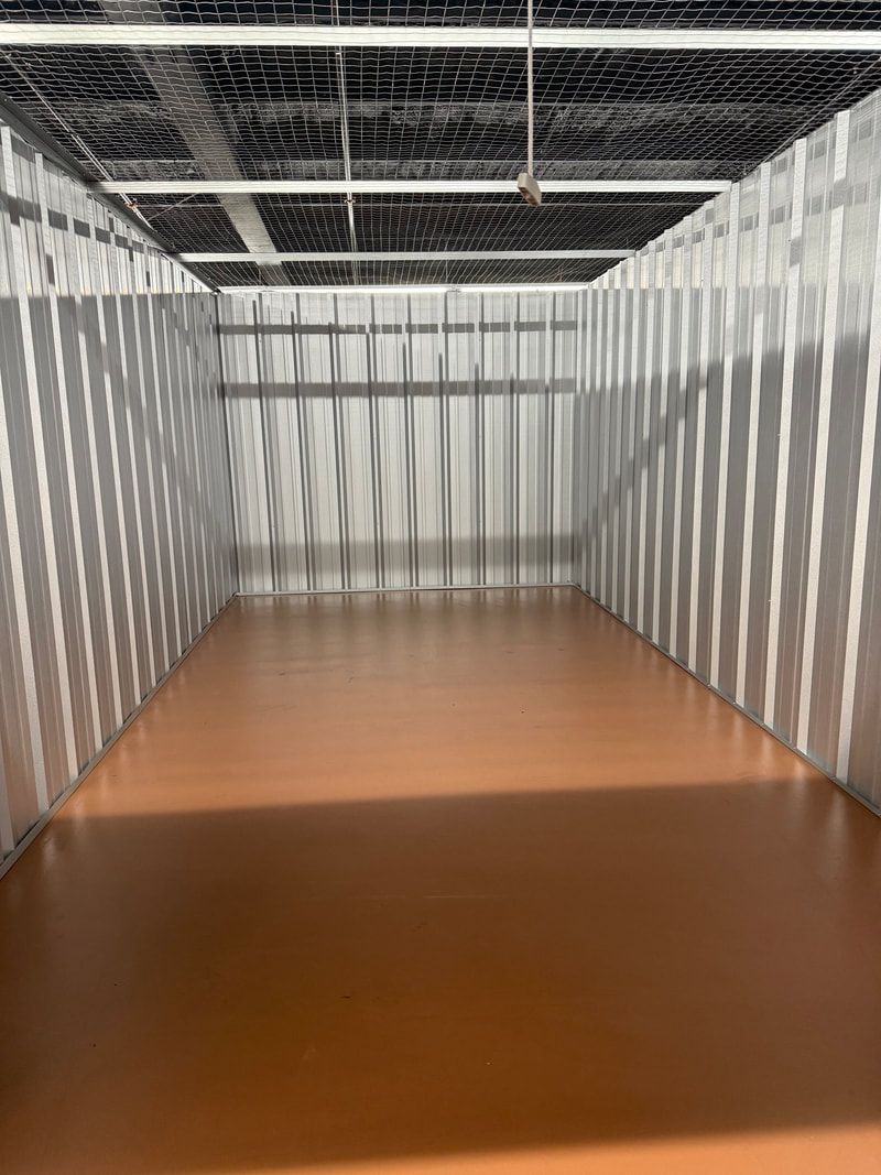 Empty storage unit with corrugated metal walls and orange floor.