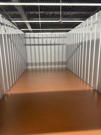 Empty storage unit with corrugated metal walls and orange floor.