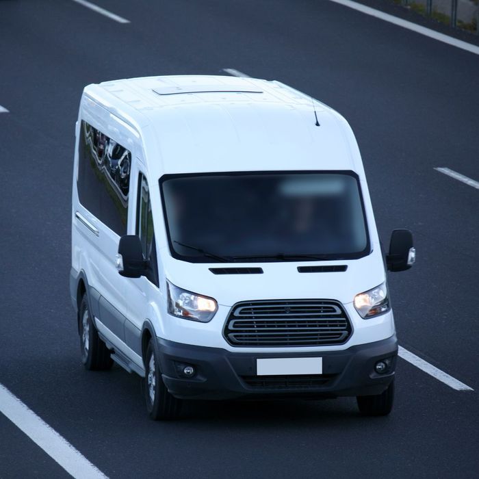 A black van is parked in a parking lot in front of a brick building.
