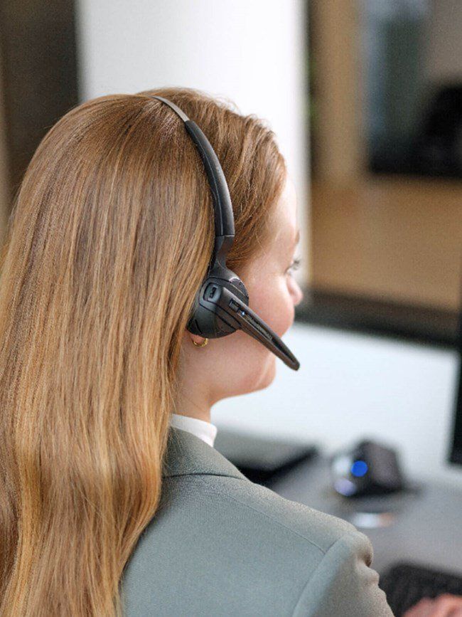 Woman with long blonde hair wearing a headset, working at a desk in an office.