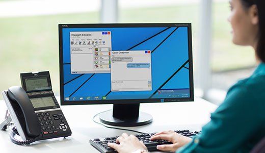 Person looking at computer with NEC SV9100 handset on desk